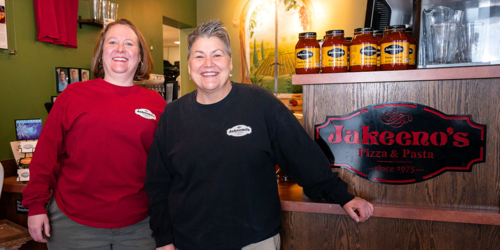 Two women standing next to a sign that reads "Jakeeno's"