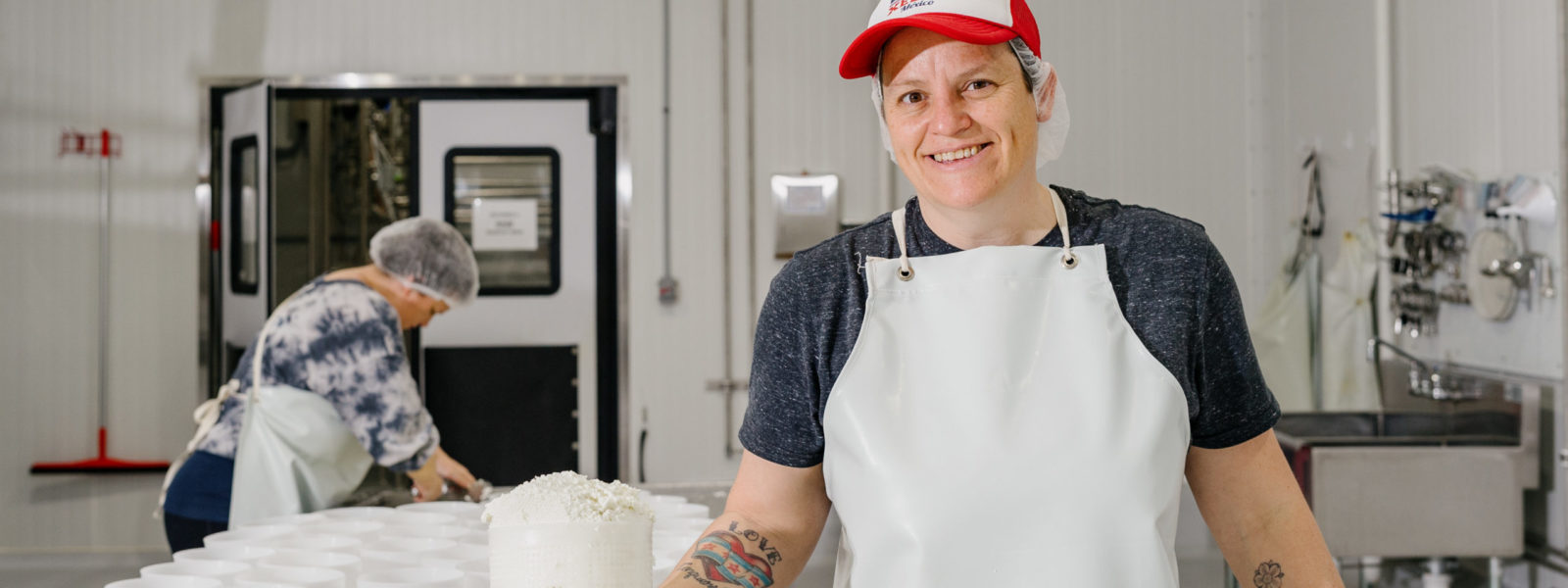 A person wearing a white apron and holding goat cheese in a creamery
