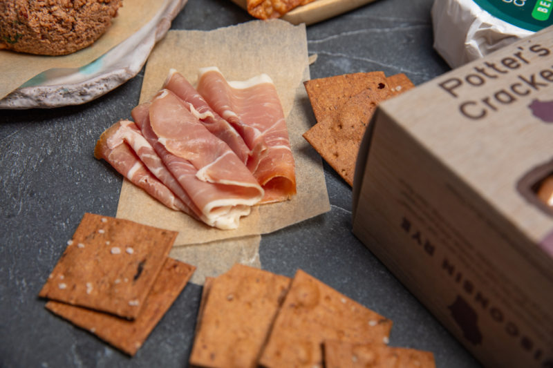 A photo of prosciutto and crackers on a slate background