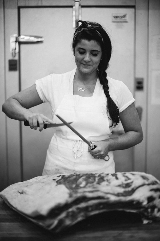 black and white image of a woman sharpening a knife over meat
