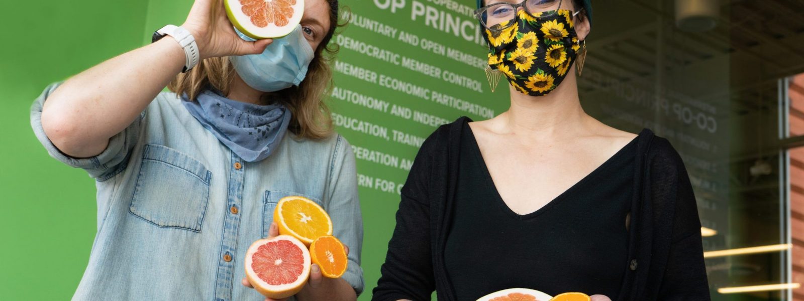 two people wearing masks holding halved citruses