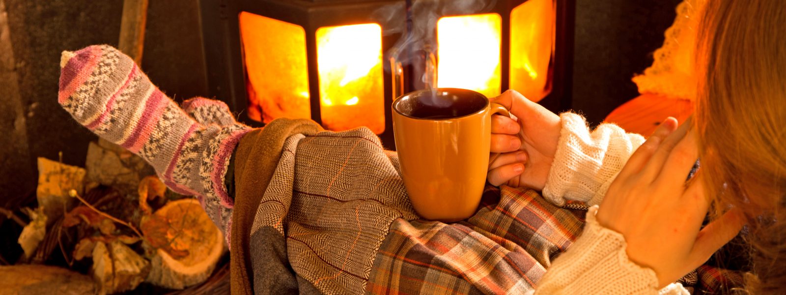 person sitting in front of a fire under a blanket with tea