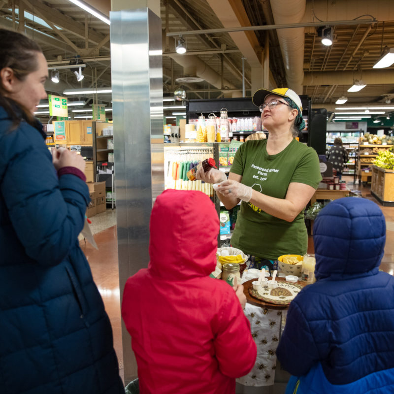 A person handing out samples of honey to a family
