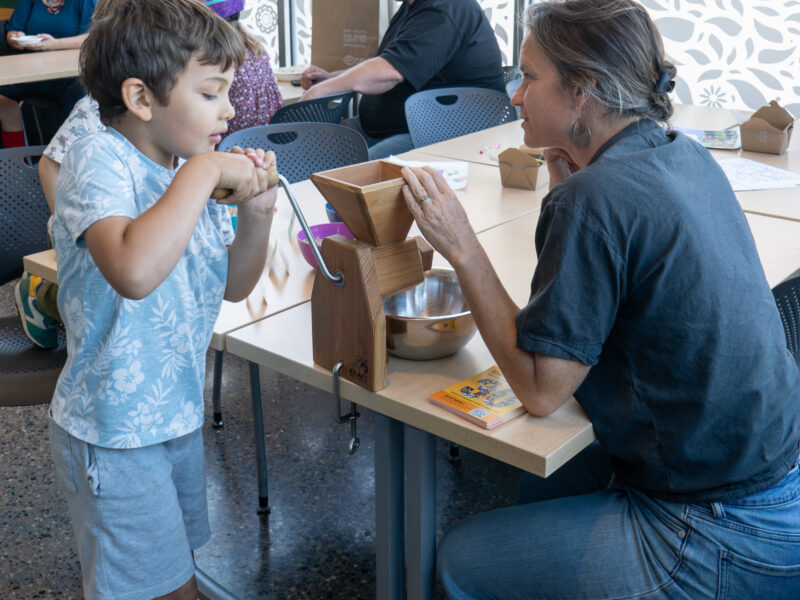 an adult helping a child with a flour mill