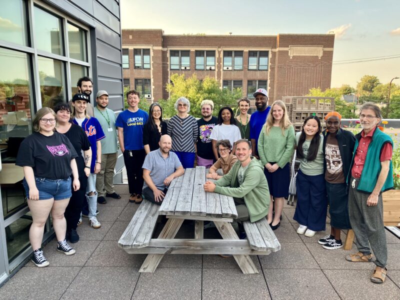 Group of people sitting and standing around a picnic table, members of the Seward Co-op Leadership and UFCW 663 bargaining team