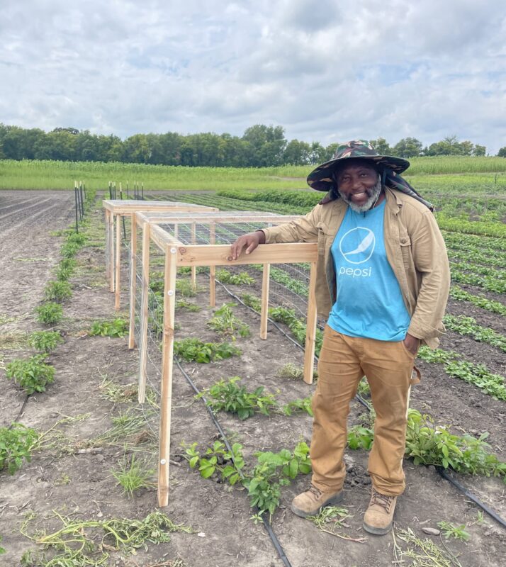 Founder of Better Greens LLC, Funwi Tati, smiles in front of a field of African vegetables
