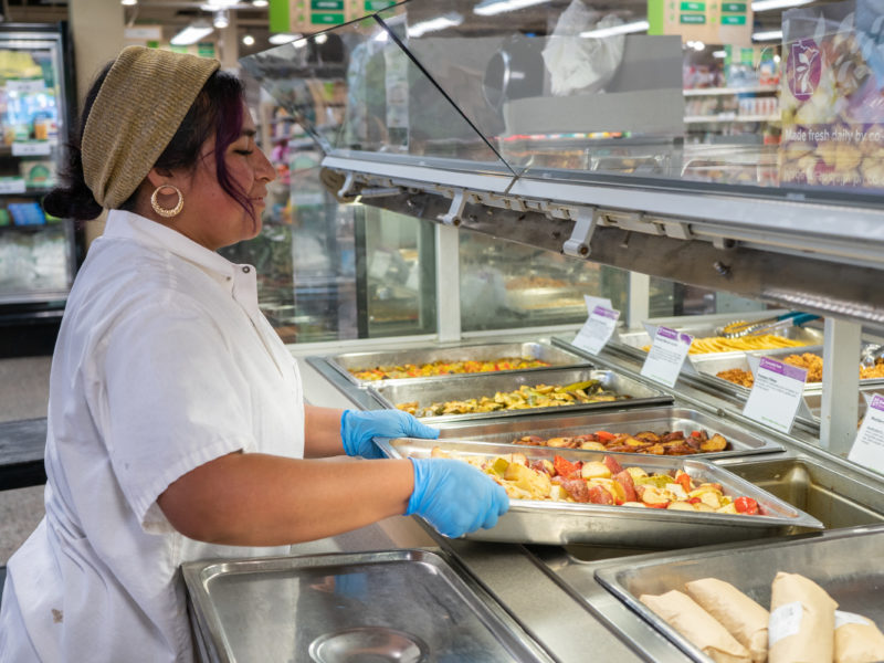 A person placing food on the Seward Co-op Hot Bar