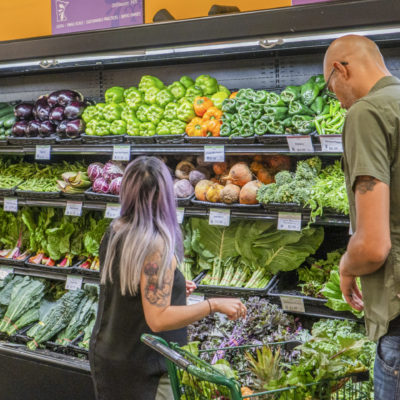 Two people shopping in front of a full produce fridge