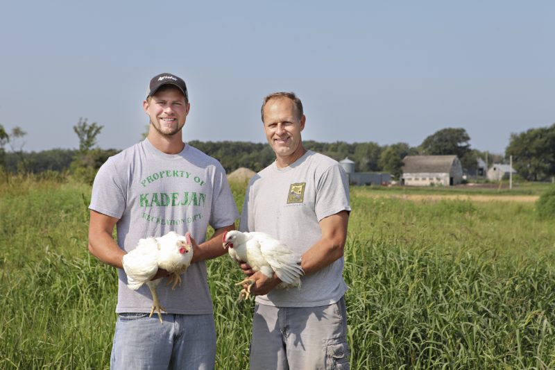 Two people holding chickens in front of a field