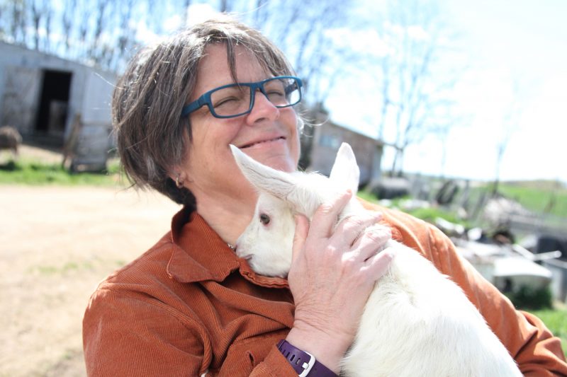 A person holding a small white goat and smiling