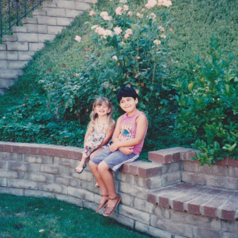 Two children sitting on a short brick wall in a backyard