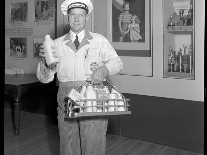 A person wearing a white hat and holding bottles of milk