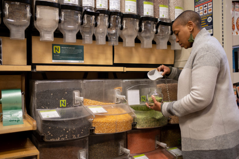 A person shopping in the bulk aisle and scooping lentils into a jar