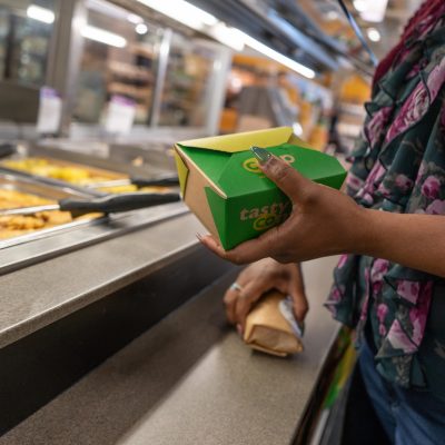 A person's hands holding a box of food at a hot bar