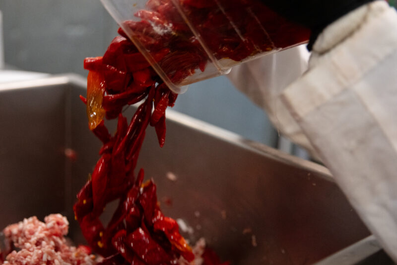 Staff adding Calabrian chili peppers to ground meat as part of the sausage making process