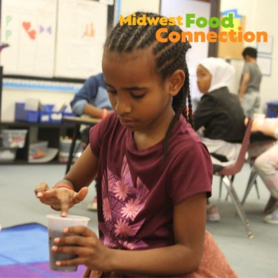 A child planting seeds in a classroom with the Midwest Food Connection logo in the top corner
