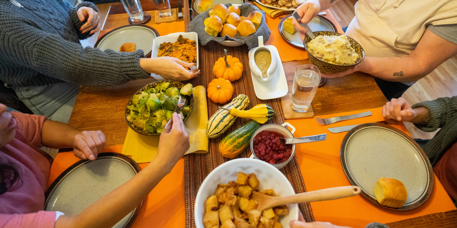 Hands passing harvest dishes around a festive table