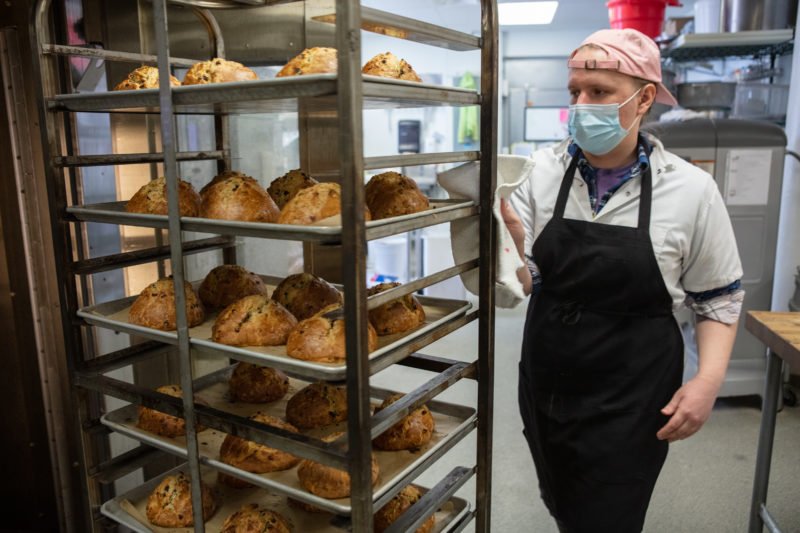 A staff member at the Seward Co-op Bakery taking bread out of the oven