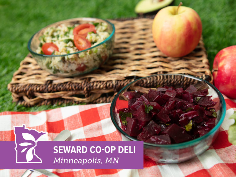 Two salads at a picnic with text overlay that reads "Seward Co-op Deli"