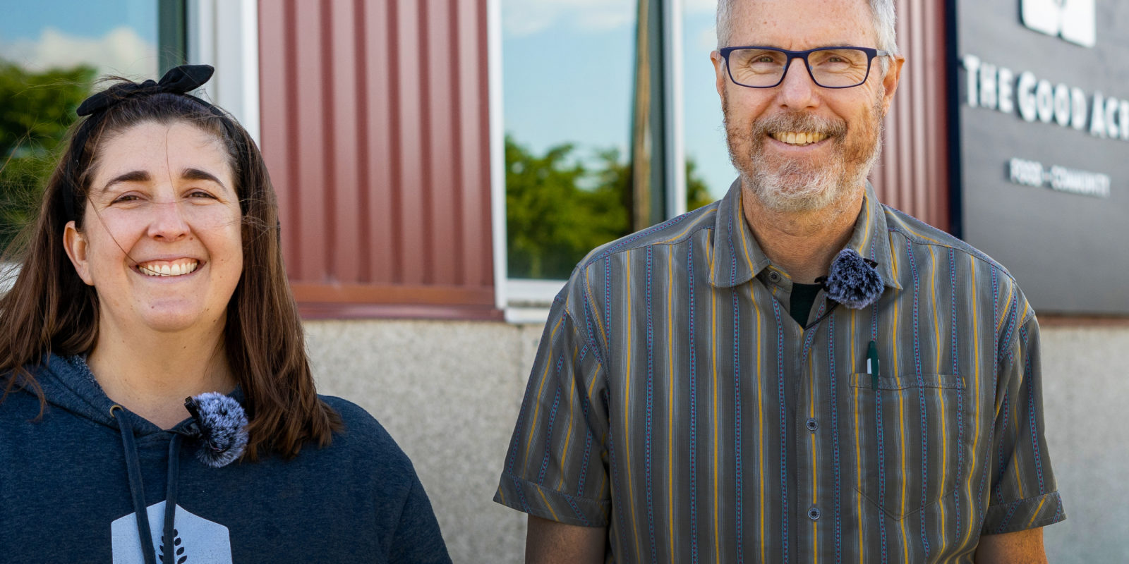 Two people smiling and standing next to a red building