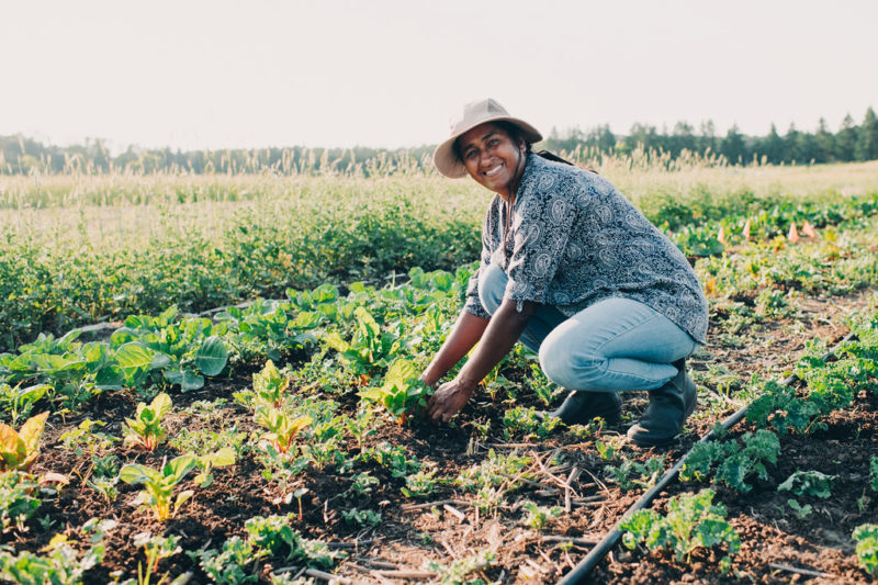 A person in a sun hat working on a farm and smiling at the camera
