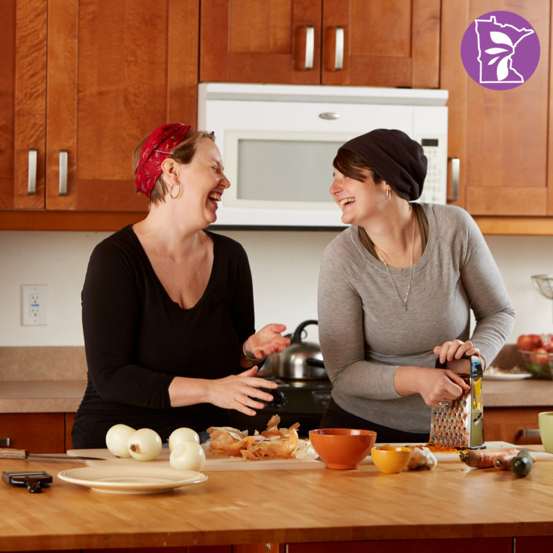Two women laughing and cooking in a kitchen