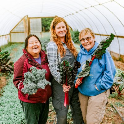 A group of people smiling and laughing while holding vegetables inside a greenhouse