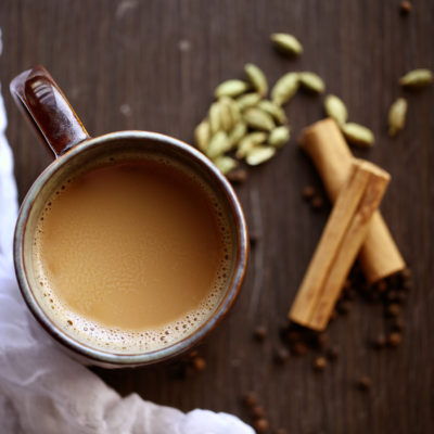 An overhead photo of a cup of chai with spices on the side