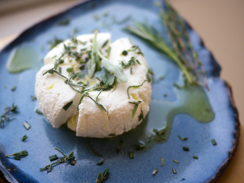 A round of chevre with herbs and oil on a plate
