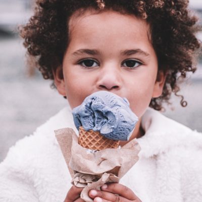 A young child eating purple ice cream from a waffle cone
