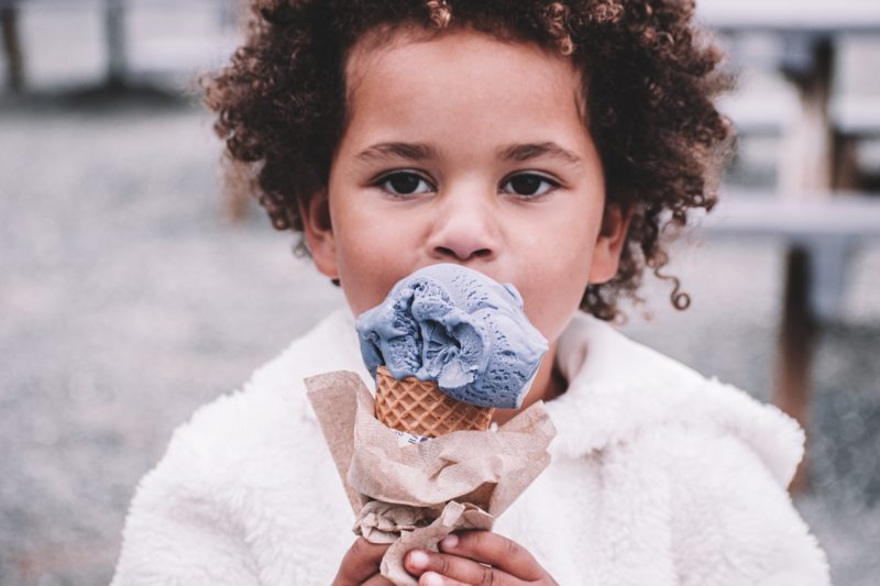 A young child eating purple ice cream from a waffle cone