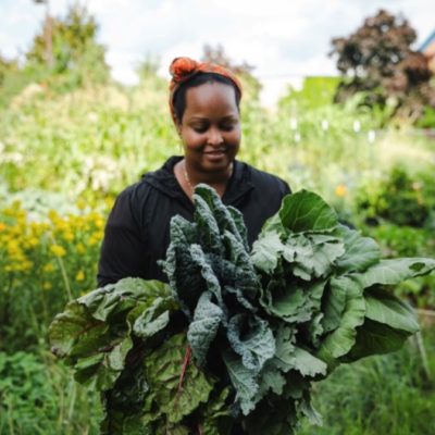 A person holding many leafy green vegetables and smiling