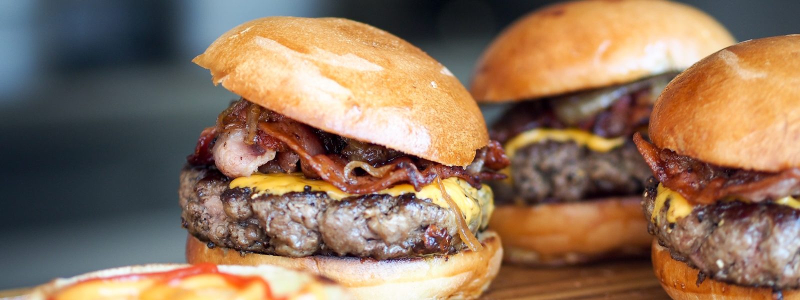 Three bacon cheeseburgers on a wooden board
