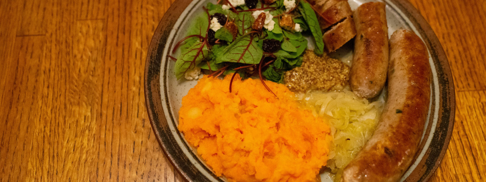 sauasage with plate of sweet potatoes, salad, and mustard