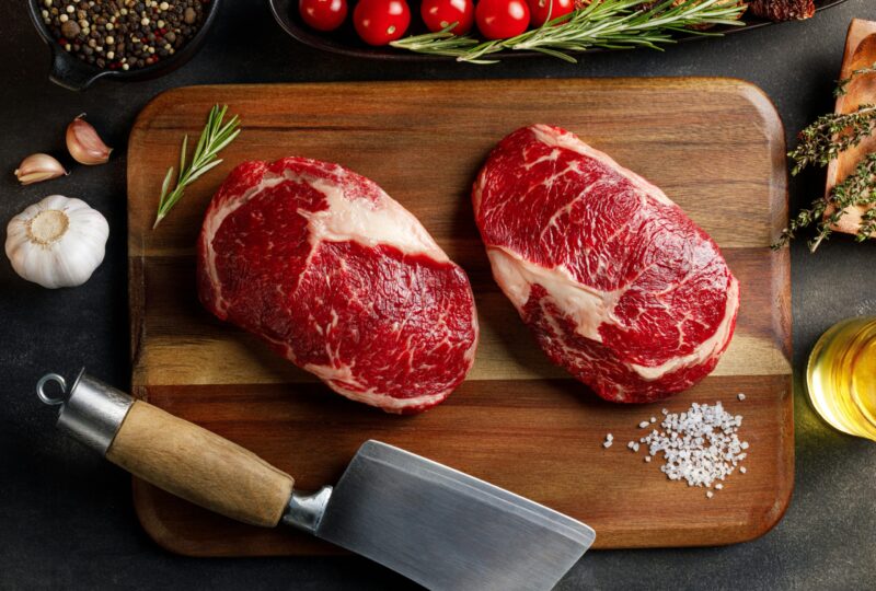 two cuts of top sirloin on wooden cutting board surrounded by spices and herbs