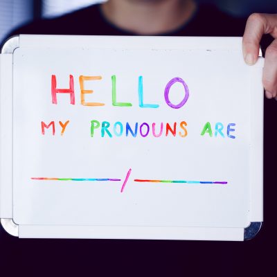 A person holding a sign that reads "Hello, my pronouns are"