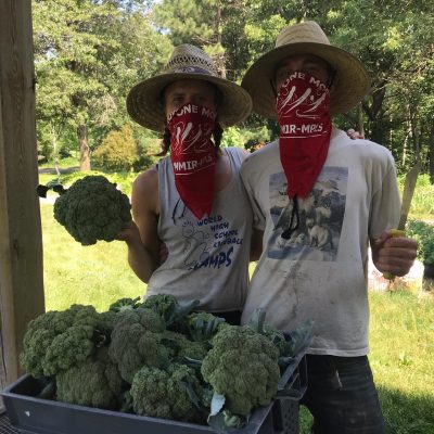 Two people wearing red bandanas and hats and holding broccoli