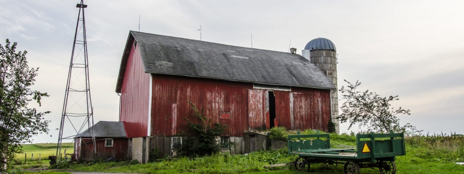 A red barn next to a green field with farming equipment