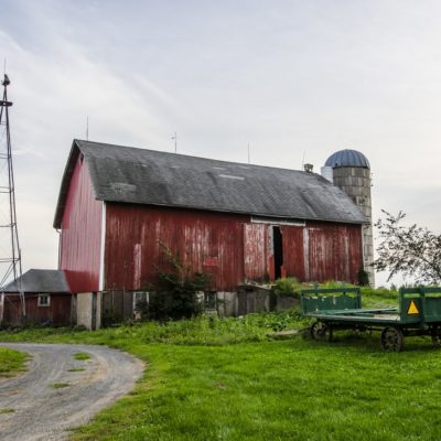 A red barn next to a green field with farming equipment