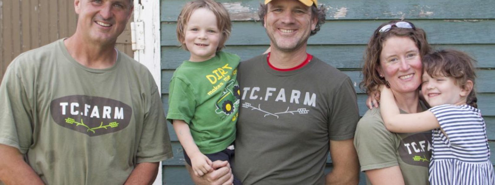 A group of people standing a smiling wearing TC Farm shirts